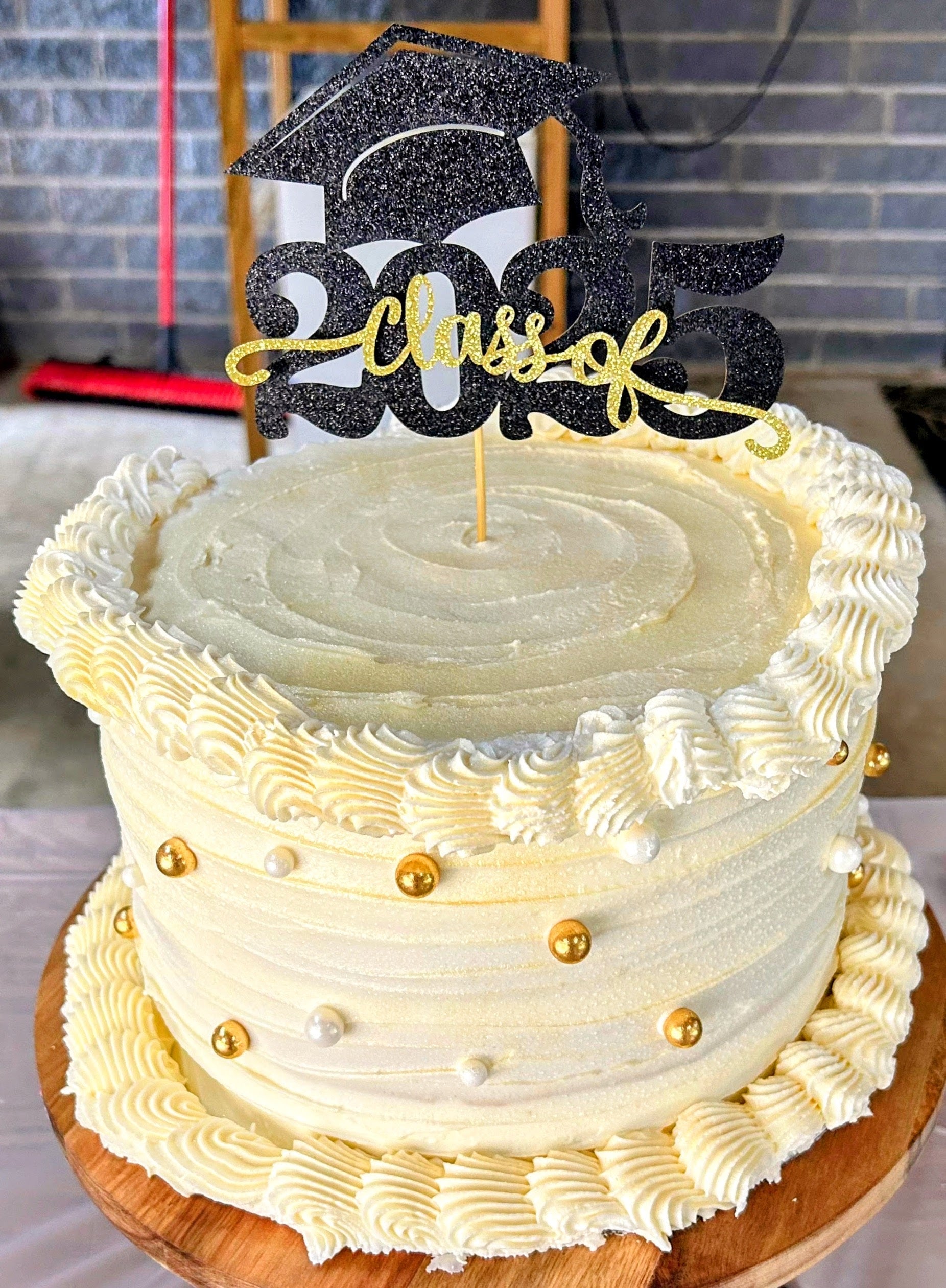 Graduation-themed cake with 'Class of 2025' topper on a wooden stand.