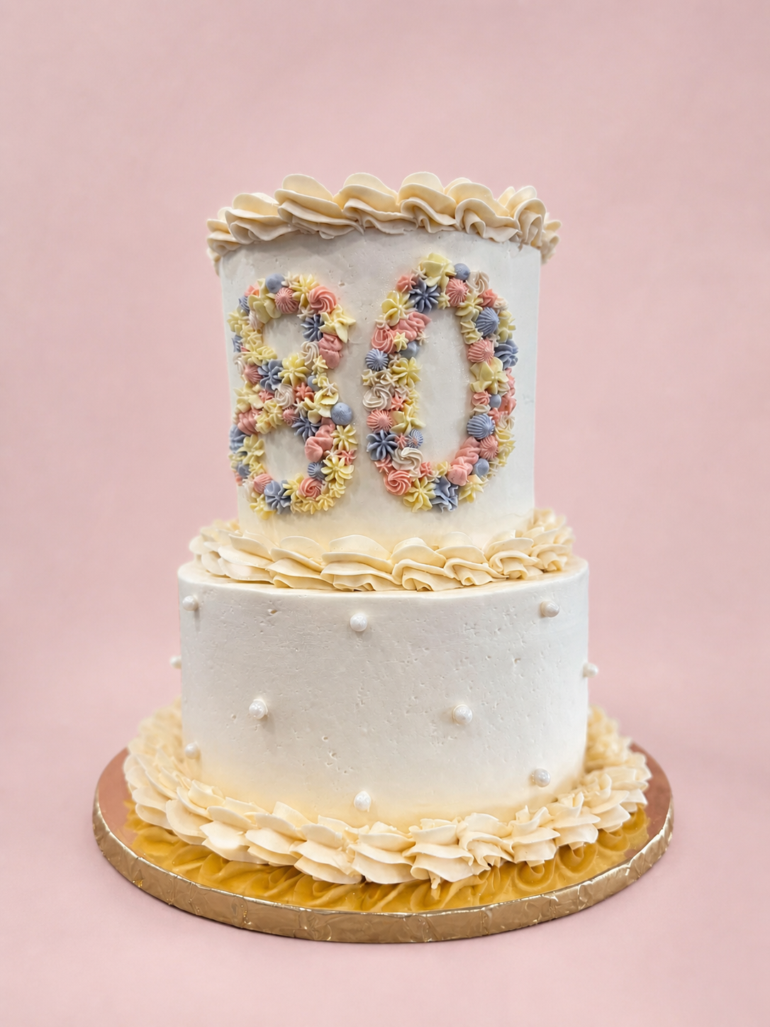 Two-tiered carrot cake flavored birthday cake with floral number 80 on a pink background