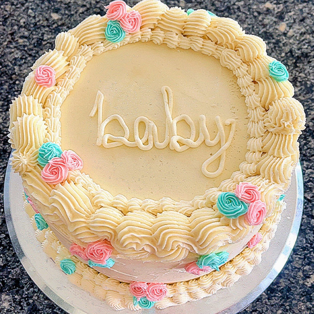 Baby gender reveal shower cake with 'baby' written on it, decorated with pink and blue roses.