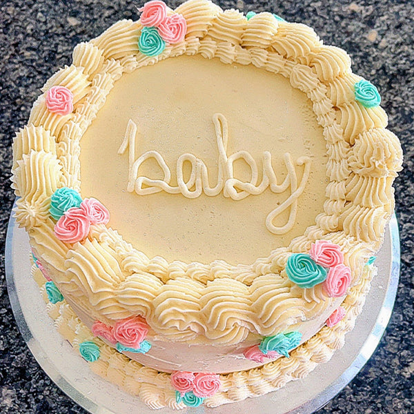 Baby gender reveal shower cake with 'baby' written on it, decorated with pink and blue roses.