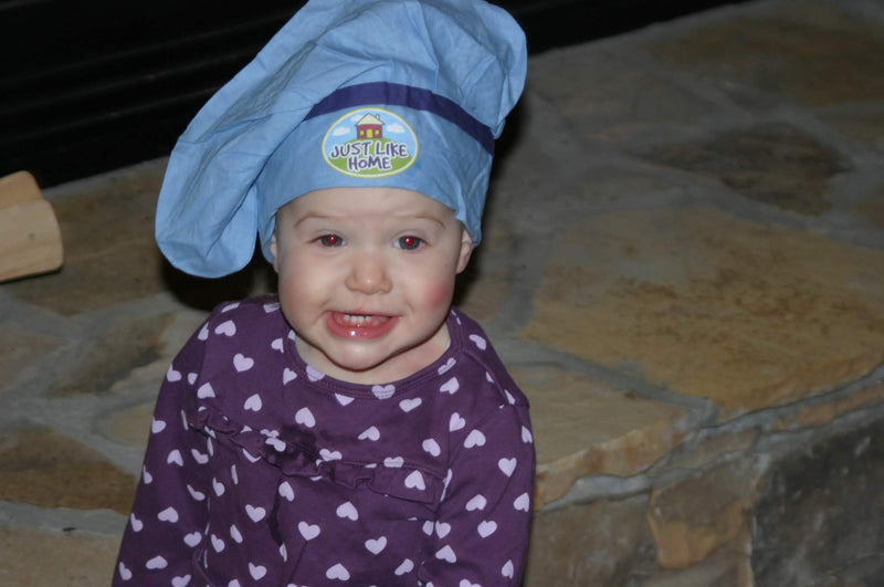 Child wearing a blue chef's hat with a logo on a stone surface