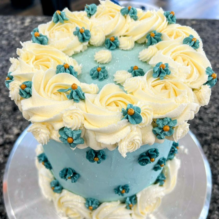 Decorative cake with white frosting, blue flowers, and a light blue center on a dark surface.