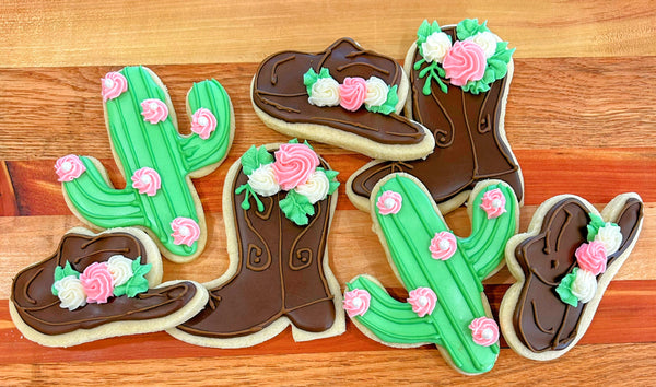 Decorative cookies shaped like cowboy boots and cacti with flowers on a wooden surface