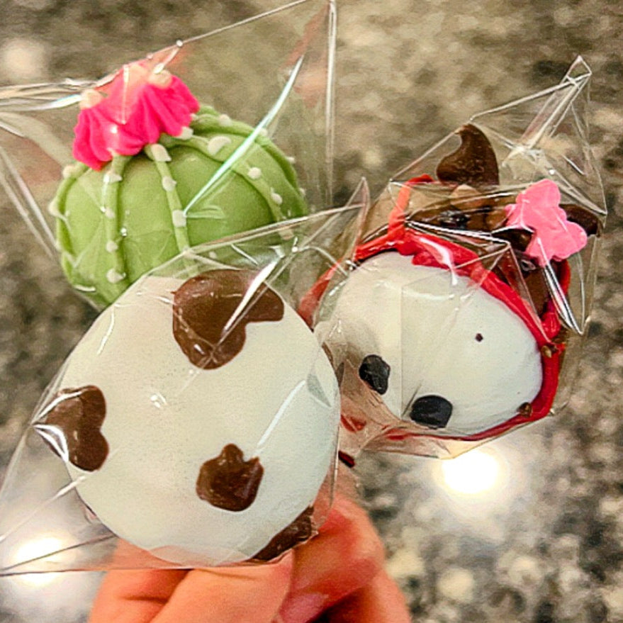Three decorative bath bombs shaped like a cactus, cow, and fox in clear plastic packaging.