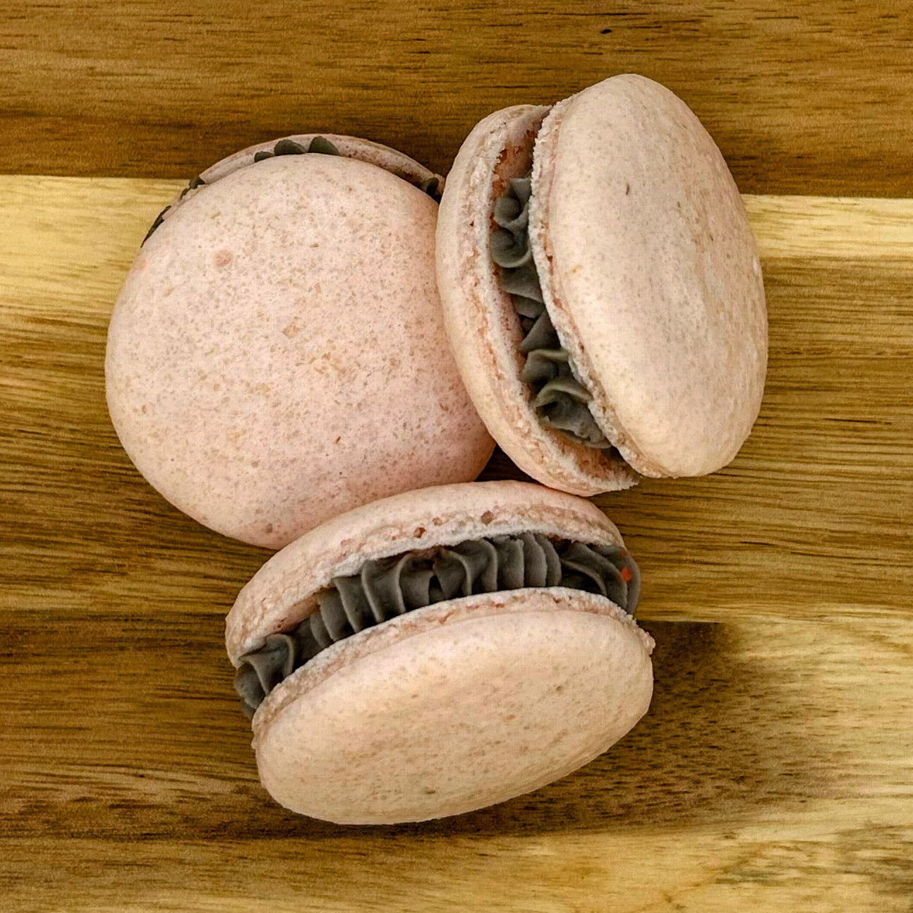 Three pink macarons with a gray filling on a wooden surface