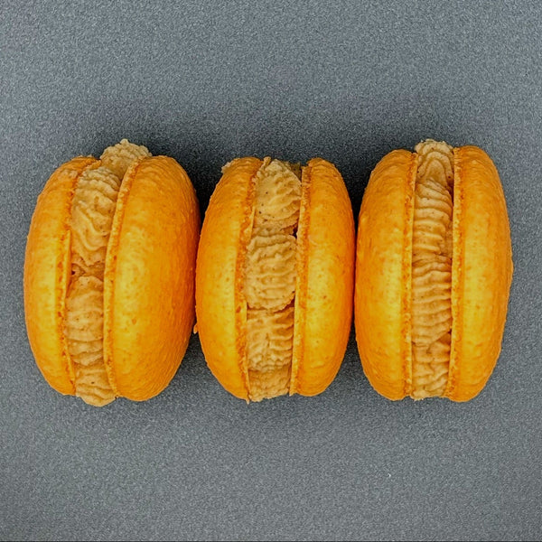 Three orange macarons on a gray background
