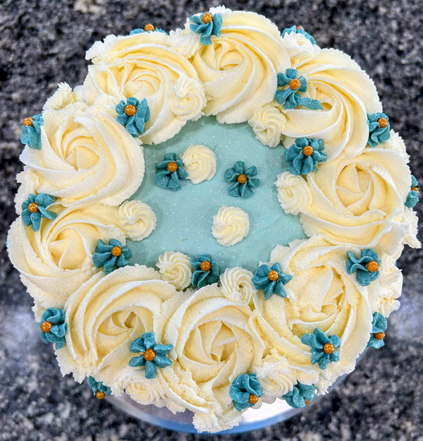 Decorative cake with white frosting, blue flowers, and a light blue center on a dark surface.