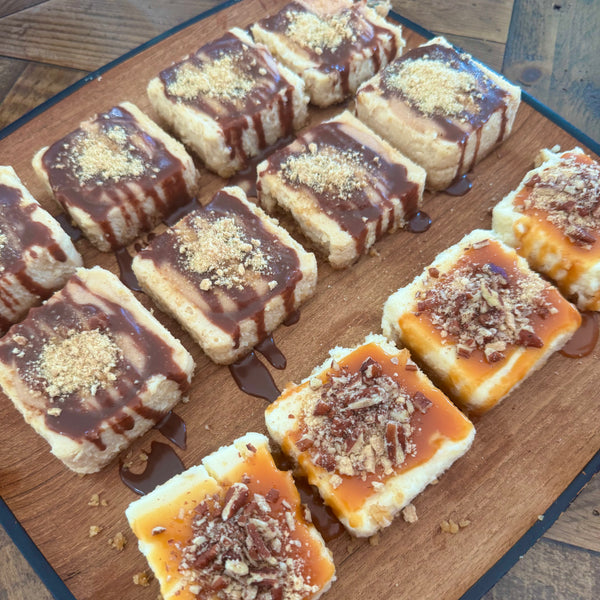 Mini square peanut butter cheesecakes with chocolate drizzle and mini square turtle cheesecakes with pecans and caramel drizzle. 