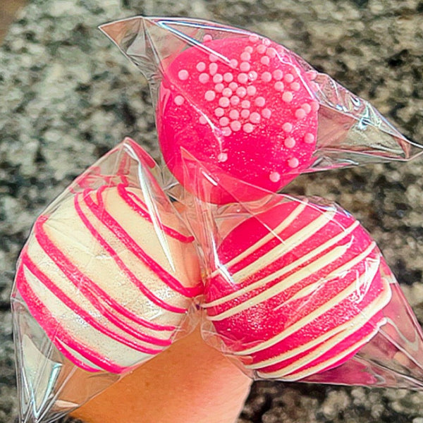 Pink and white striped bath bombs in clear plastic packaging on a granite surface.