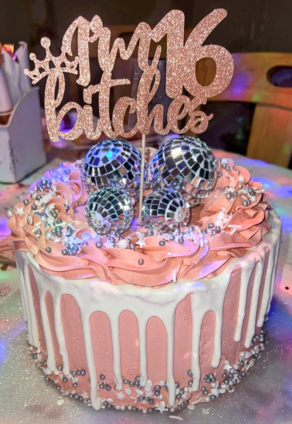 Pink cake with disco balls and '16 bitches' topper on a blurred background