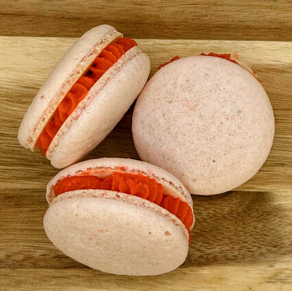 Three macarons with orange filling on a wooden surface