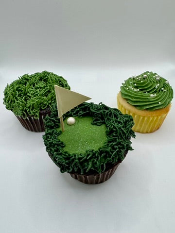 Three chocolate and vanilla flavored cupcakes with vanilla buttercream frosting decorated to resemble a golf course (with green grass, a flag, and ball), and grass. 