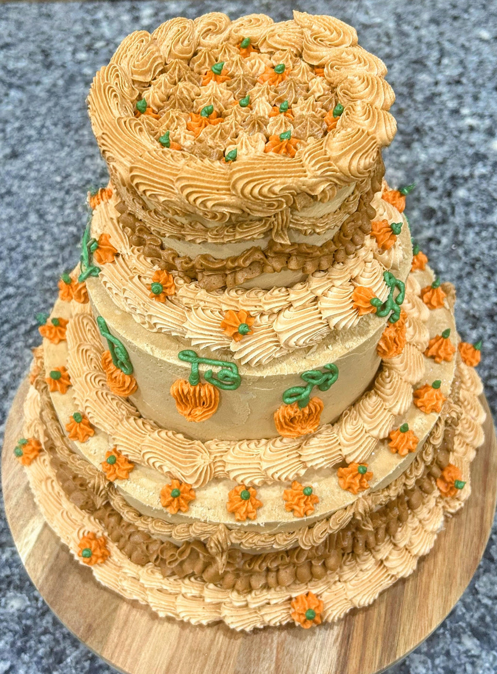 Three-tiered cake with decorative frosting and small pumpkins on a textured surface