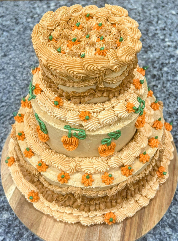 Three-tiered cake with decorative frosting and small pumpkins on a textured surface